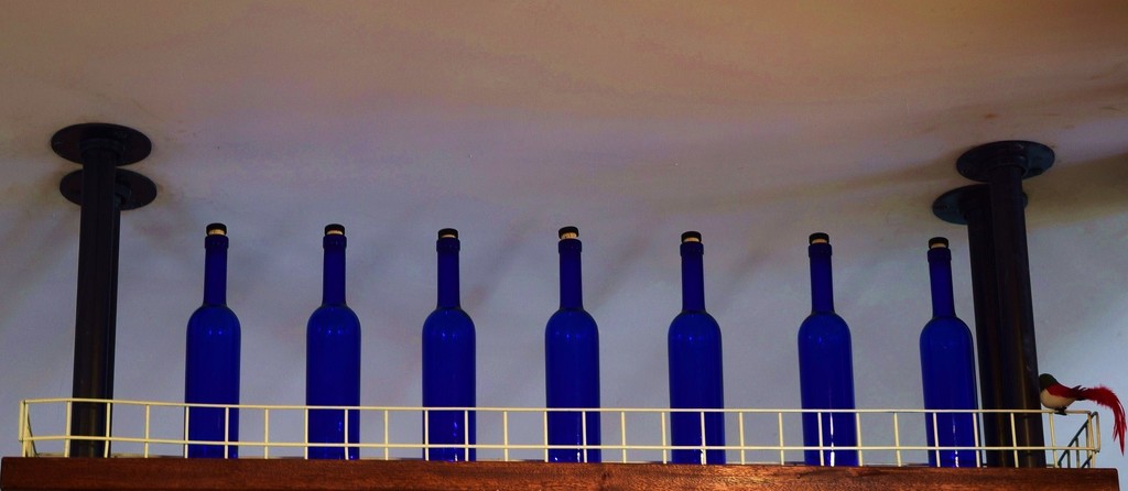 7 Blue Bottles sitting on a High Shelf. by happysnaps