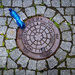 Manhole cover, cobble stones  & blue bottle 